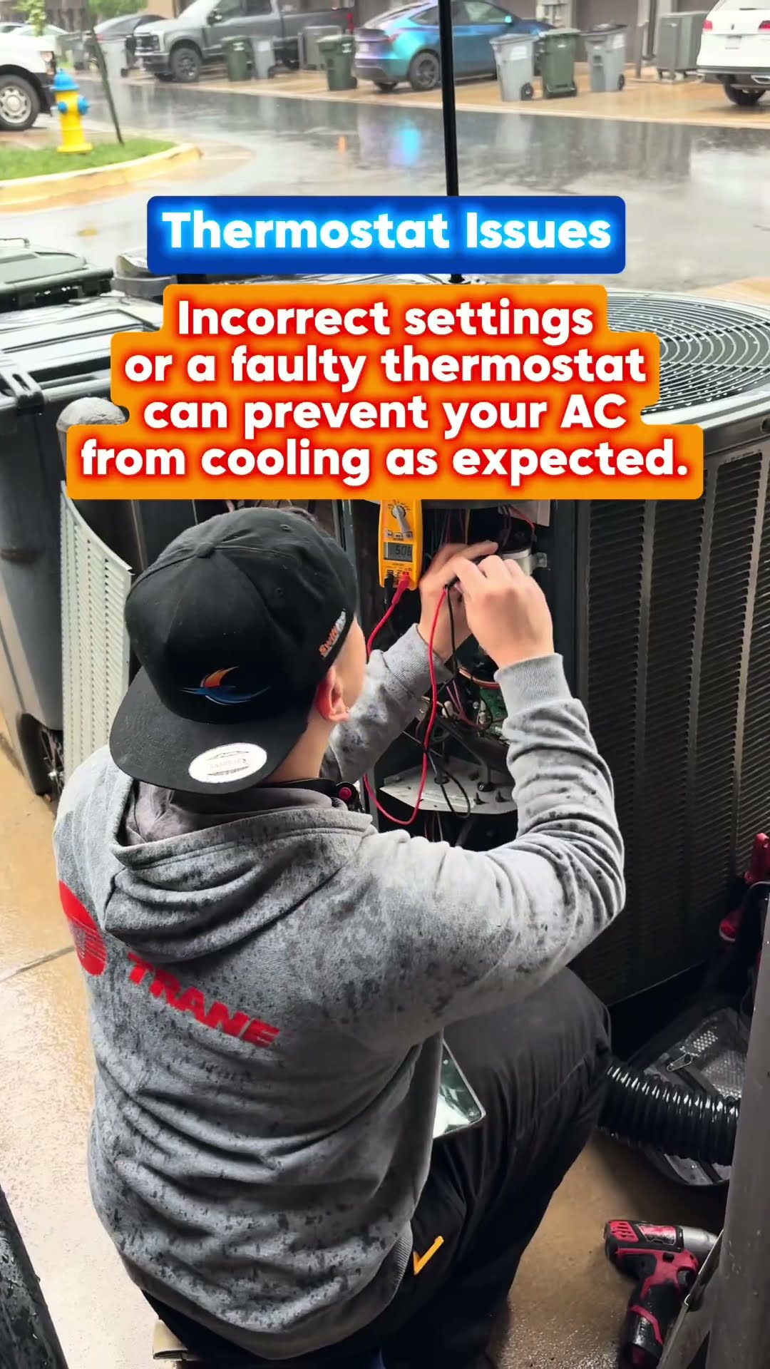 AC troubleshooting at a townhouse condenser in the rain: a tech checks refrigerant with gauges at the service valves, a tech in a Trane hoodie tests wiring with a multimeter at a Trane condenser, and