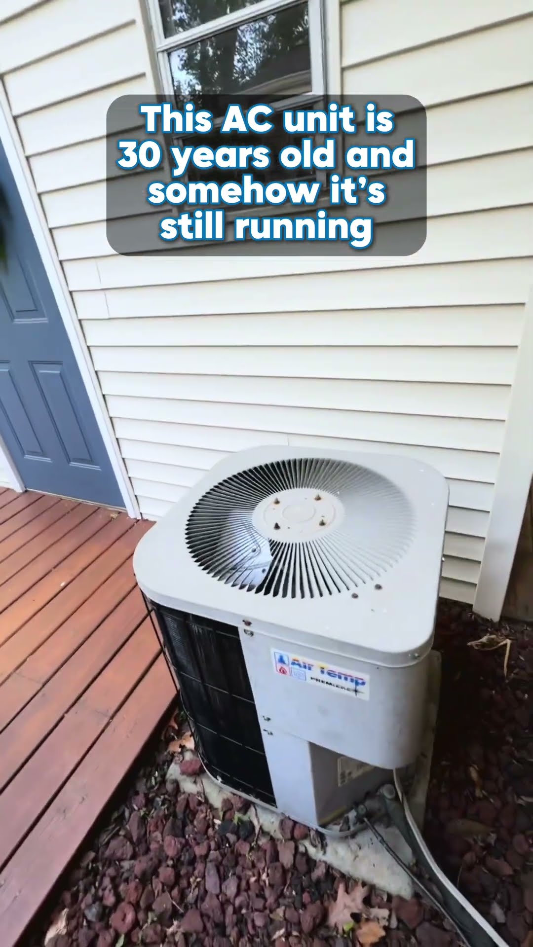 A 30-year-old Air Temp Premiere AC condenser, still running, sits on red lava rock beside a house's siding and wooden deck.