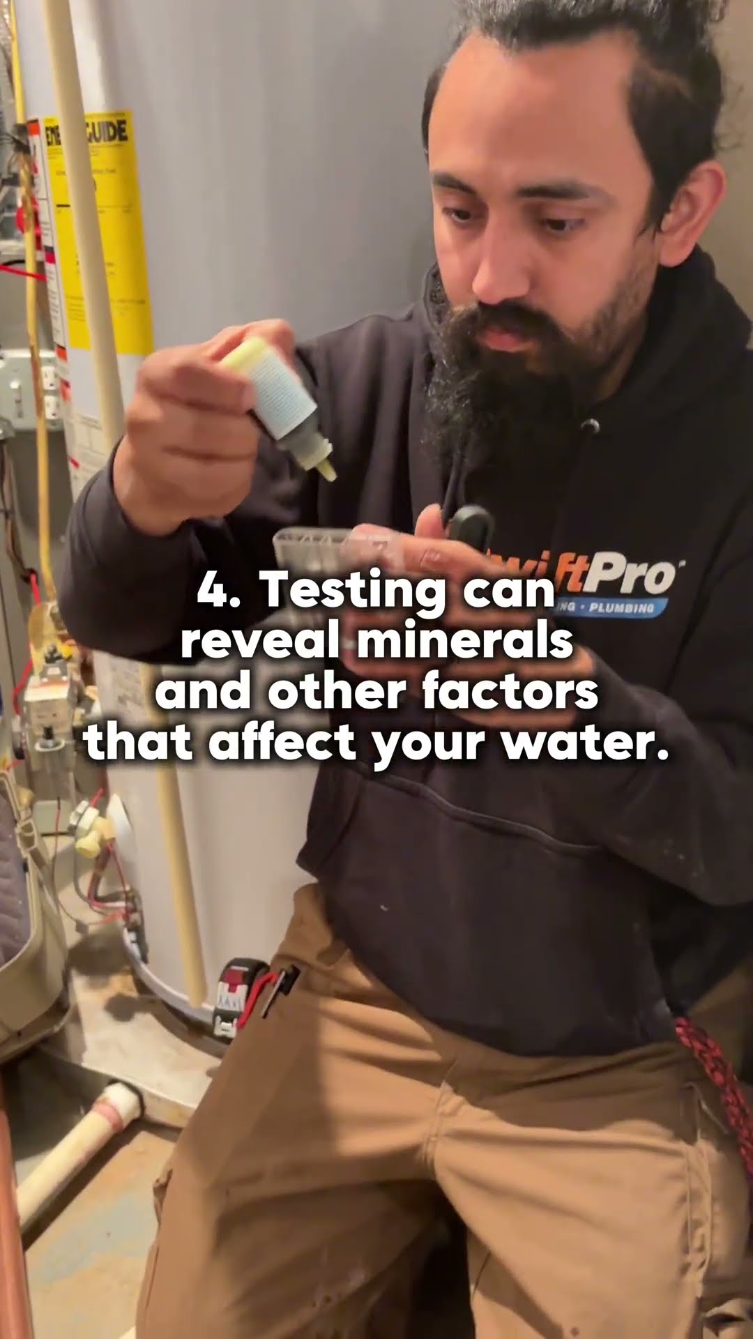 A tech kneels beside a water heater in a utility room and runs a drop-reagent water test kit.