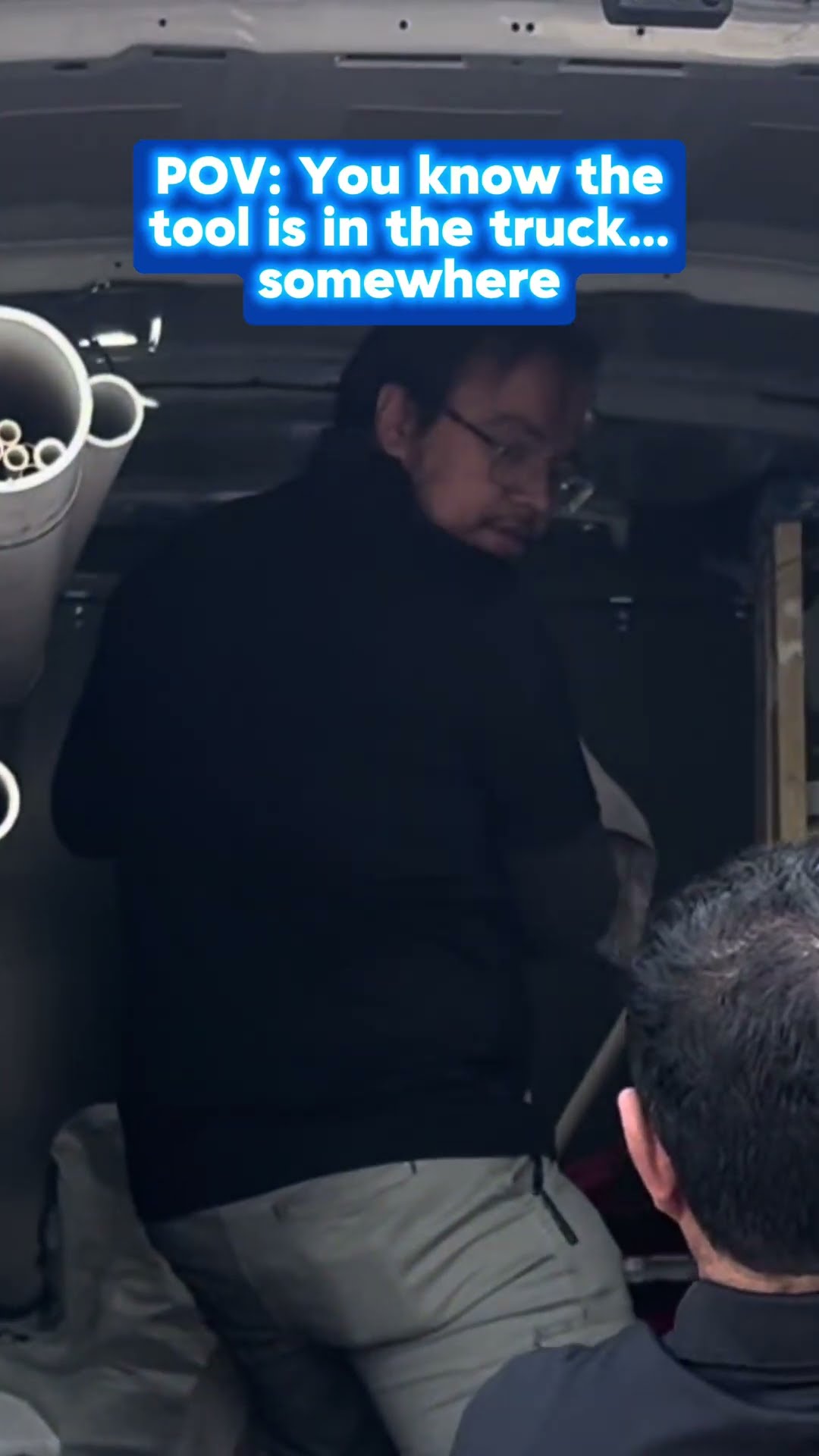 A tech in a black polo and khakis digs through the back of a service van with a red Milwaukee case and hand truck, and a tech in glasses searches inside the van.