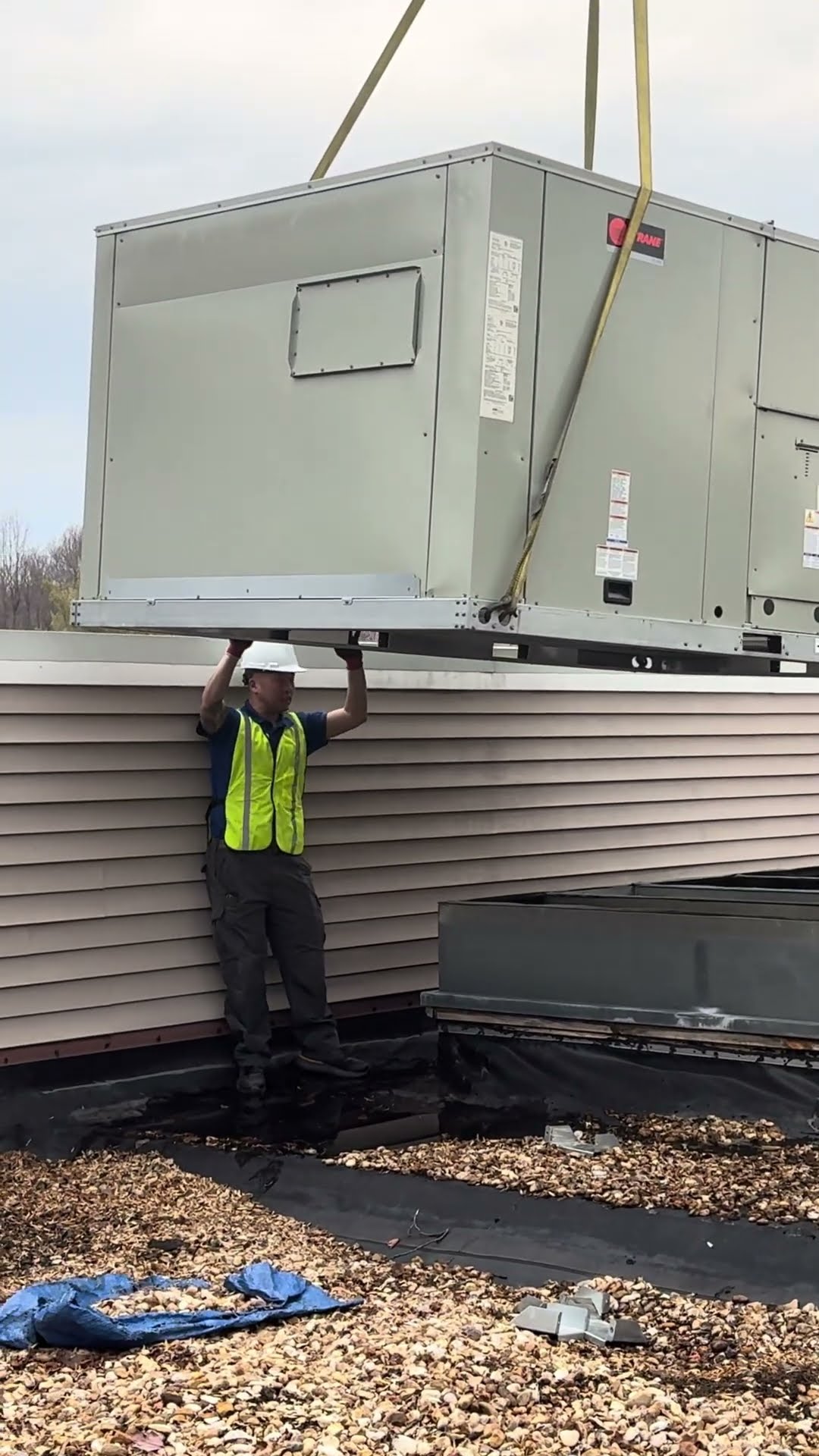 A crane lifts a commercial packaged rooftop unit over a parking lot (SwiftPro truck parked below) onto a flat gravel roof.